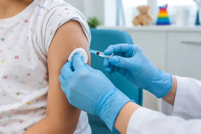 Çocuk kliniğinde sağlık çalışanı küçük bir çocuğun koluna aşı uyguluyor.